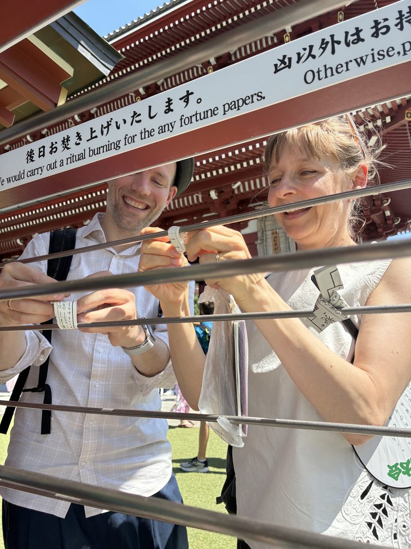 Guests laughing beside the rack for fortune papers at a shrine