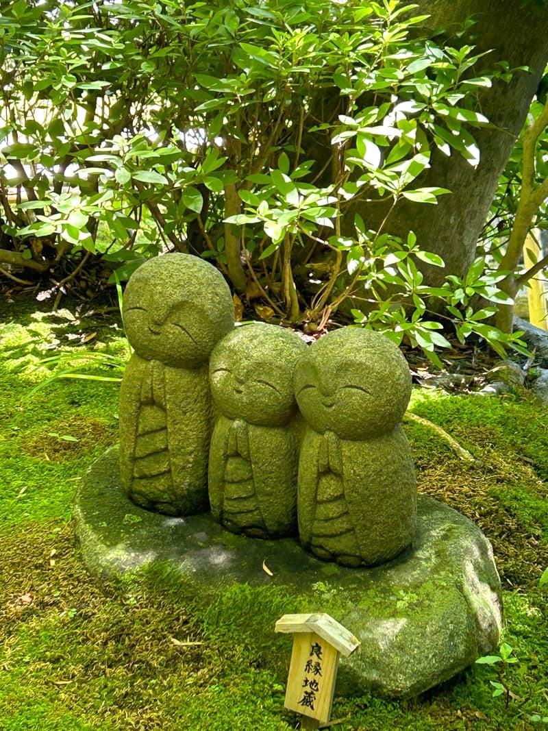 Three small stone Jizo statues wearing red bibs beside a path