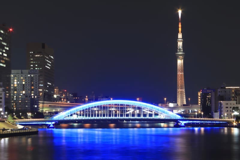 Tokyo Skytree lit at night above a bridge reflected in the river