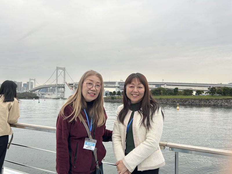 Two licensed guide interpreters aboard a yakatabune boat in Tokyo Bay, with the Rainbow Bridge behind them